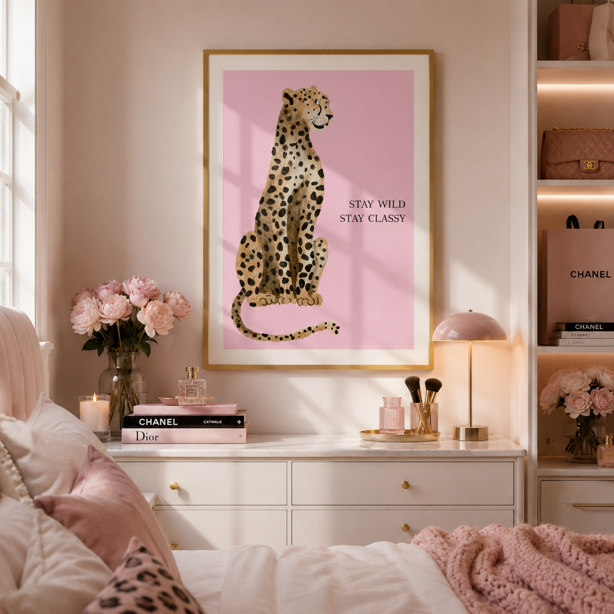 A framed art print featuring a spotted leopard on a pink background with the text 'STAY WILD STAY CLASSY' is displayed on a bedroom wall above a white dresser. The room is styled with pink bedding, a pink lamp, and decorative items, including a Chanel shopping bag on the shelf to the right.