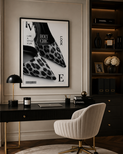 A framed fashion poster featuring a black and white leopard print shoe with the text 'HOLY CHIC' and 'LOOK', displayed on a beige wall above a dark desk with a cream ribbed chair in a styled interior.