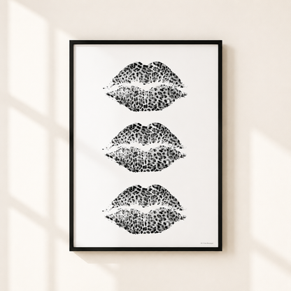 A framed wall art print featuring three vertical rows of black leopard-print lips on a white background, hung on a light beige wall with soft window shadows.