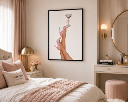 A framed wall art print featuring a stylized illustration of legs in pink high heels holding a martini glass, displayed above a neatly made bed in a softly styled bedroom.