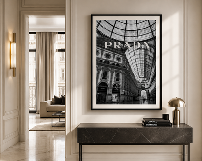 A framed black and white art print of the Prada Galleria shopping arcade, styled on a cream wall above a dark marble console table with a gold lamp.