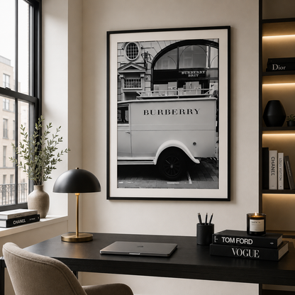 A framed black and white art print of a vintage Burberry lorry hanging on a beige wall above a dark desk in a modern, stylishly decorated room.