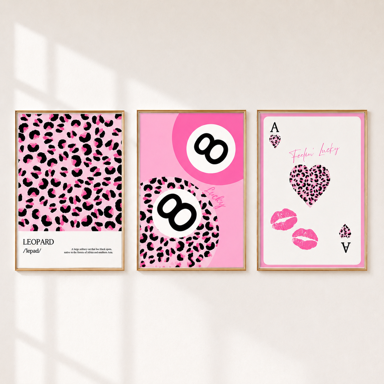 Three framed fashion-themed art prints with pink leopard print and pink graphics, displayed side-by-side on a light beige wall with soft window shadow overlays.
