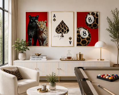 Three framed wall art prints hang above a white credenza in a styled living room. The left print shows a black panther and leopard on red; the center print is an aces of spades with leopard print details; the right print shows leopard print billiard balls on red.