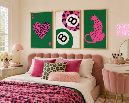 A styled bedroom featuring three framed wall art prints above a bed. The prints have bold pink and green leopard-print designs: a heart on the left, billiard balls in the center, and a cat on the right.