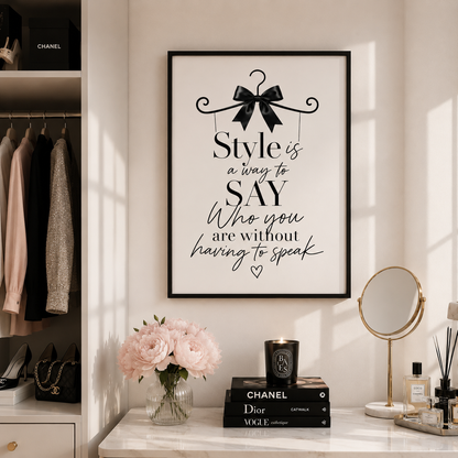 A framed wall art print with elegant black typography and a black bow illustration on a white background, displayed in a styled room above a marble console table with flowers, books, and a mirror.