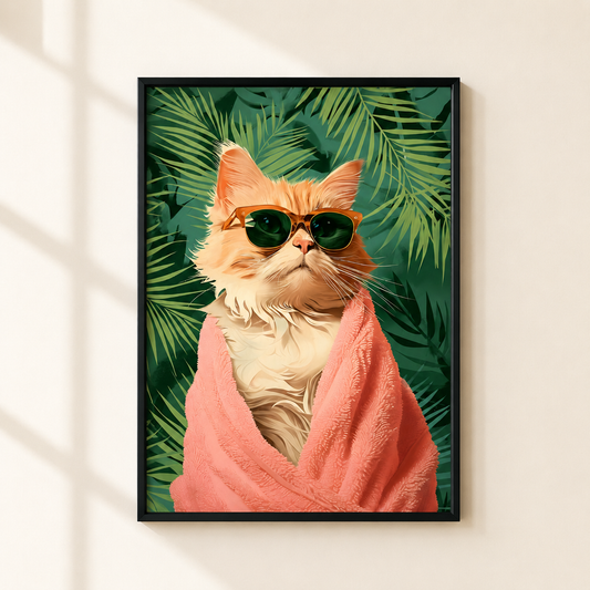 A framed art print featuring an orange tabby cat wrapped in a pink towel and wearing dark sunglasses, set against a background of green tropical leaves. The framed print is mounted on a light beige wall with soft window shadow patterns.