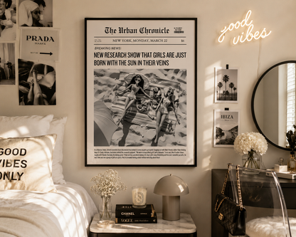 A framed black-and-white newspaper-style wall poster reading 'The Urban Chronicle' hangs on a beige wall in a styled bedroom. The room includes a bed with pillows, a side table with a lamp and vase, a mirror, and a neon sign reading 'good vibes'.
