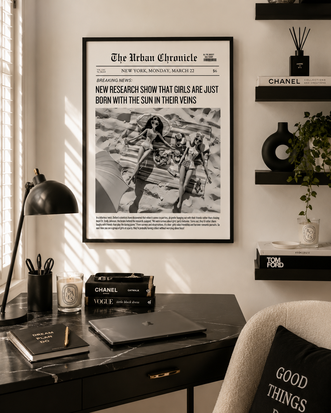 A framed black-and-white newspaper-style wall print reading 'The Urban Chronicle' hangs above a dark desk in a styled home office. The scene includes a black desk lamp, books, shelves, a plant, and part of a chair, with warm sunlight casting shadows across the room.