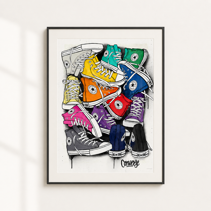 A framed art print featuring a colorful illustration of stacked Converse high-top sneakers on a white background, hung on a light wall.