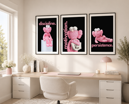 A styled home office interior featuring three framed wall art prints hanging above a desk. The prints show pink cartoon-style figures on a black background with the words 'discipline.
