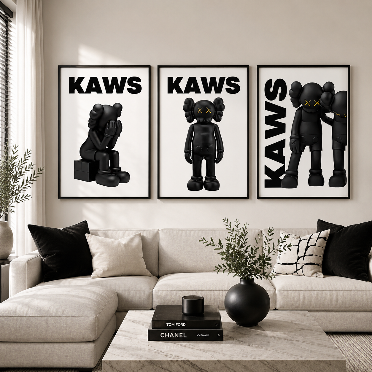 Three framed black and white KAWS art prints displayed on a beige wall above a modern white sectional sofa in a styled living room.