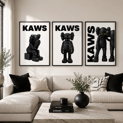 Three framed black and white KAWS art prints displayed on a beige wall above a modern white sectional sofa in a styled living room.