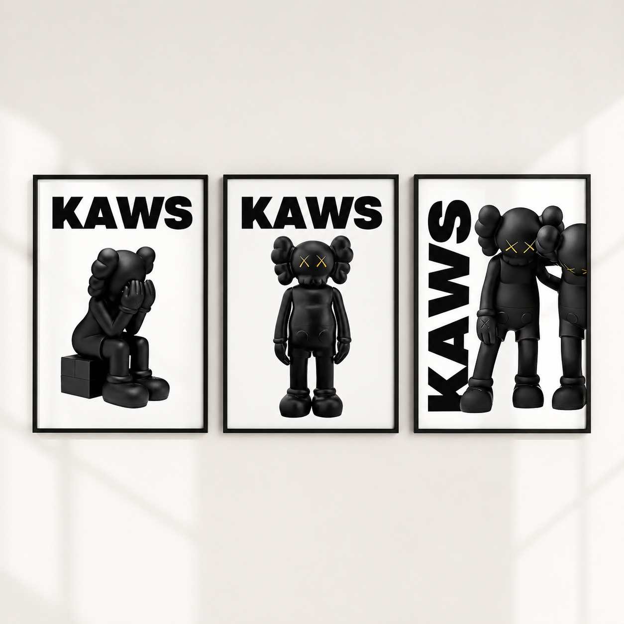 Three framed wall art prints featuring black KAWS character illustrations on a white background, hung side by side on a light wall.