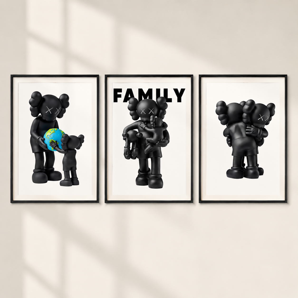 Three framed wall art prints showing stylized black cartoon figures in family-themed scenes, mounted on a light beige wall with soft window-shadow lighting.
