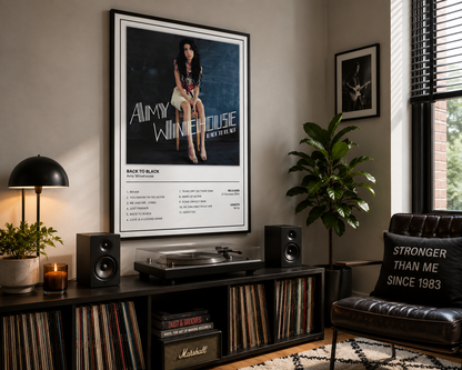 A framed Amy Winehouse 'Back To Black' music poster hangs on a wall in a styled living room setting above a record console with speakers, a turntable, and vinyl records.