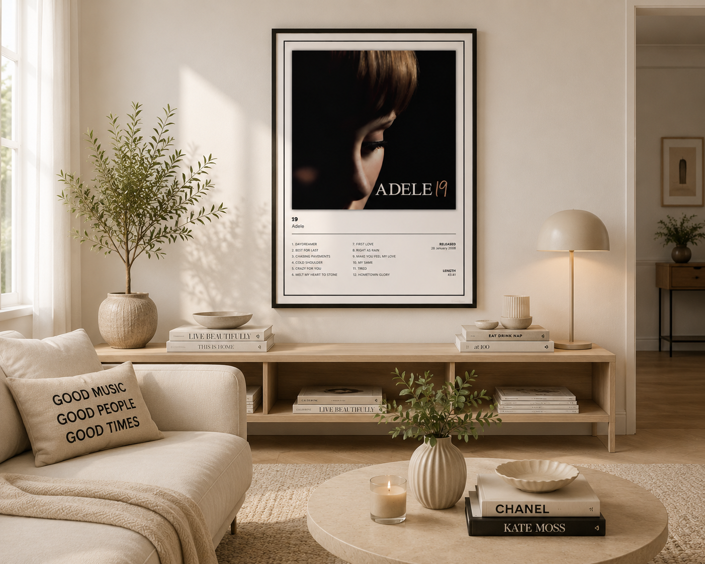 A framed Adele poster hangs on a beige wall in a modern, sunlit living room with a sofa, console table, lamp, and decorative plants.