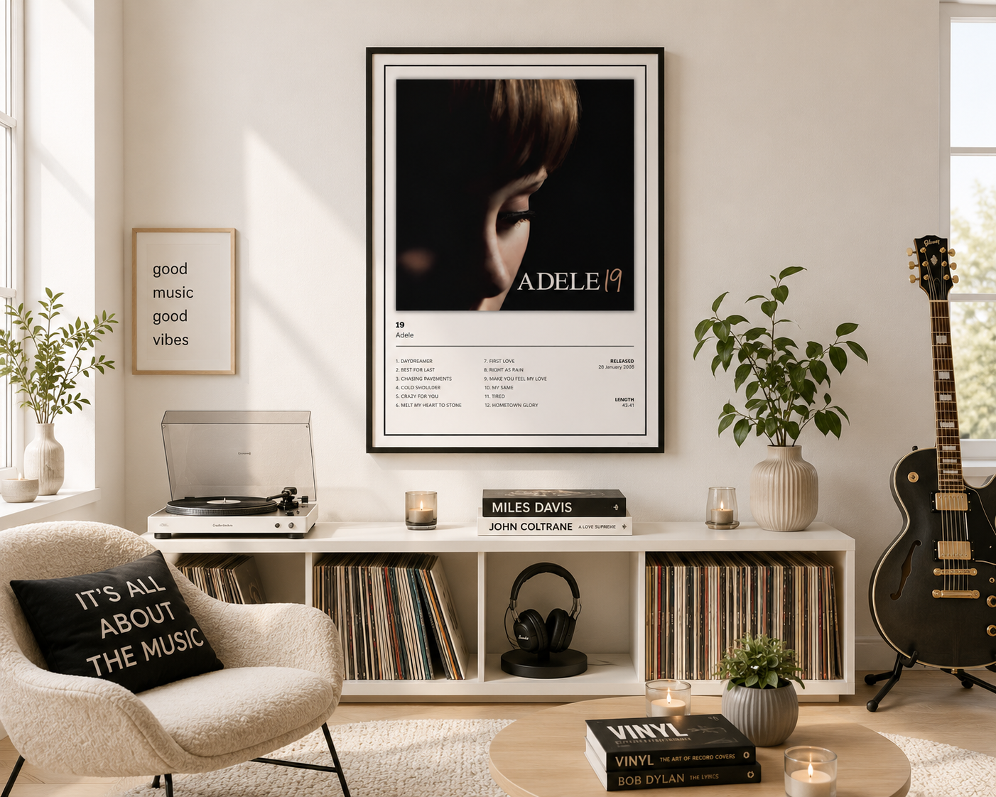 A framed Adele 19 music poster hangs on a light beige wall in a styled room with a record shelf, vinyl records, a turntable, a guitar, and a cream armchair.