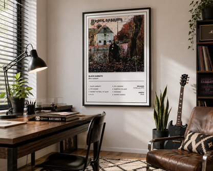 A framed Black Sabbath poster hangs on a beige wall in a styled home office setting with a wooden desk, lamp, chair, guitar, and bookshelves.