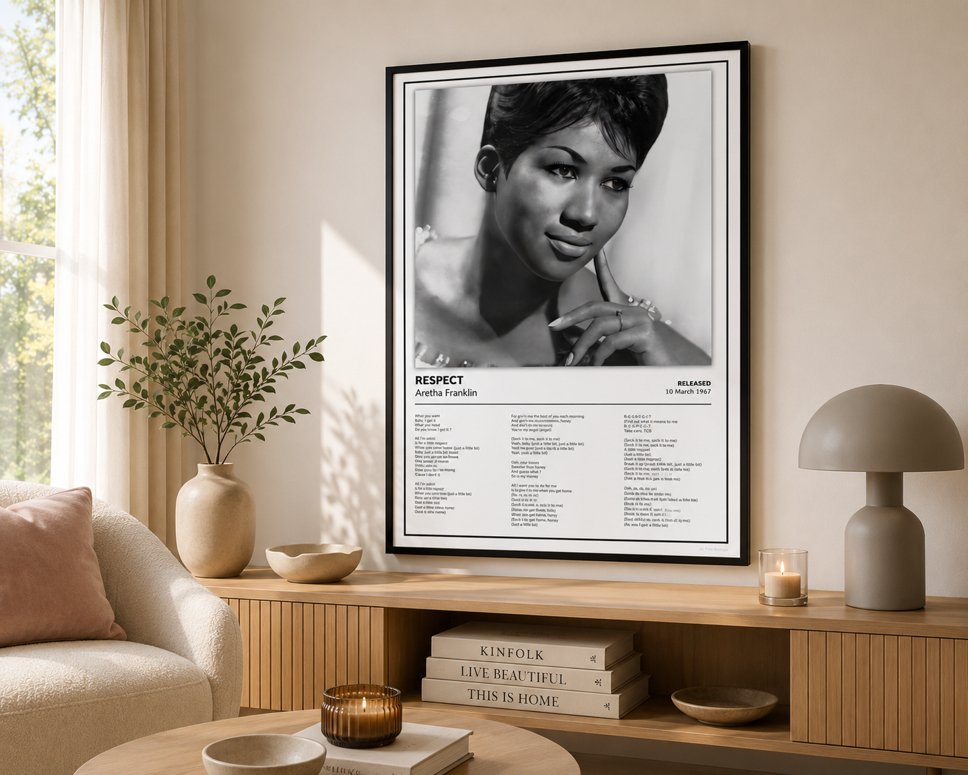 A framed black-and-white poster of Audra Anderson hanging on a beige wall in a styled living room with a sofa, lamp, and wooden console.