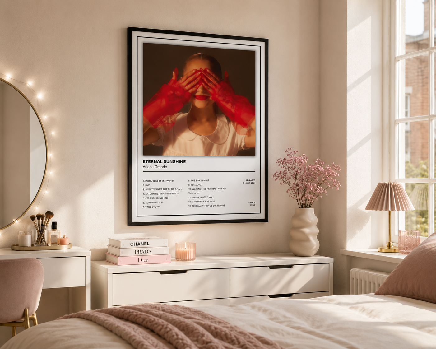 A framed wall art print hanging above a bed in a softly styled bedroom. The print features a portrait of a person with red gloves covering their eyes, with the text 'ETERNAL SUNSHINE' and song details below.