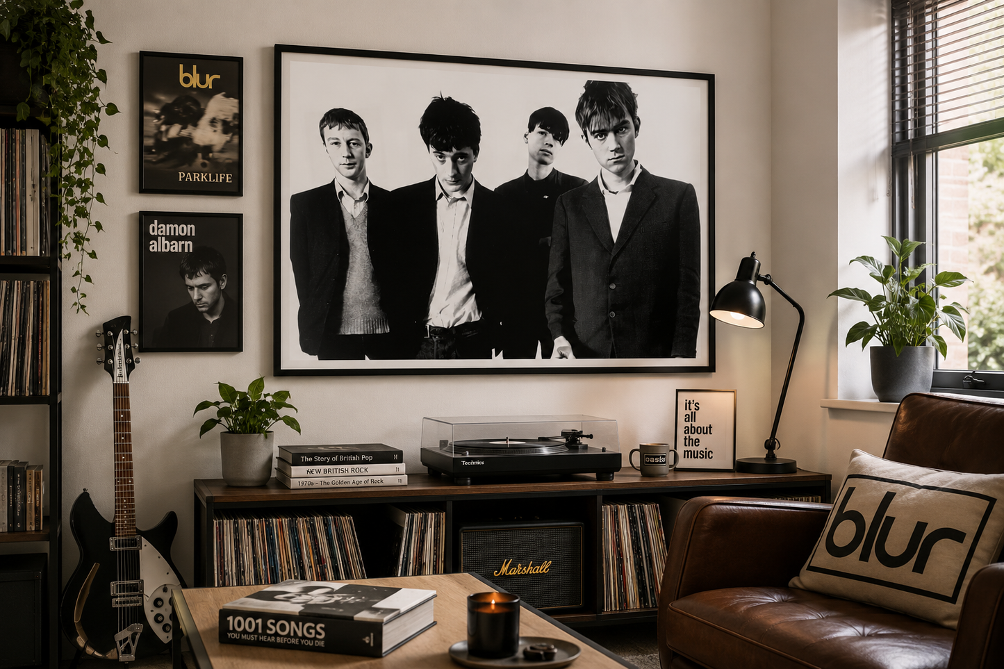 A large black and white framed poster of the band Blur hangs on a beige wall in a styled living room. The room features a brown leather sofa with a matching pillow, a wooden record player, a guitar, and other framed Blur album art.