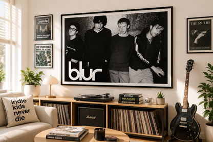 A large black and white framed poster of the band Blur hangs on a beige wall in a styled living room. The room features a wooden record console with vinyl records, a Marshall speaker, a black electric guitar, and a beige sofa with a decorative pillow.
