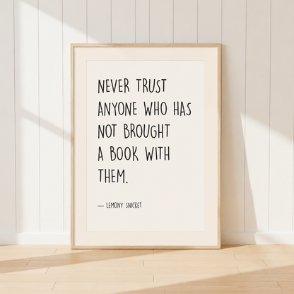 Minimalist Lemony Snicket quote print featuring the words "Never Trust Anyone Who Has Not Brought A Book With Them" in black typography, finished with a warm ivory mount and light oak frame, perfect for reading rooms and home libraries.