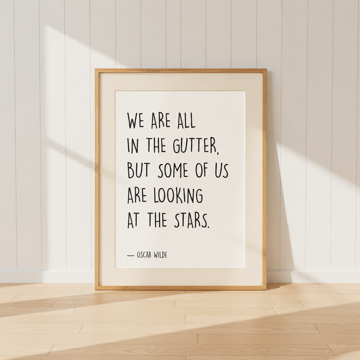 Minimalist Oscar Wilde quote print featuring the words "We Are All In The Gutter, But Some Of Us Are Looking At The Stars" in black typography, finished with a soft natural mount and light oak frame, perfect for home libraries and reading rooms.