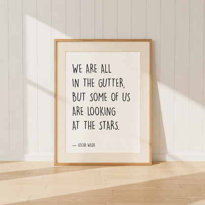 Minimalist Oscar Wilde quote print featuring the words "We Are All In The Gutter, But Some Of Us Are Looking At The Stars" in black typography, finished with a soft natural mount and light oak frame, perfect for home libraries and reading rooms.