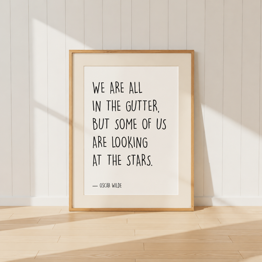 Minimalist Oscar Wilde quote print featuring the words "We Are All In The Gutter, But Some Of Us Are Looking At The Stars" in black typography, finished with a soft natural mount and light oak frame, perfect for home libraries and reading rooms.