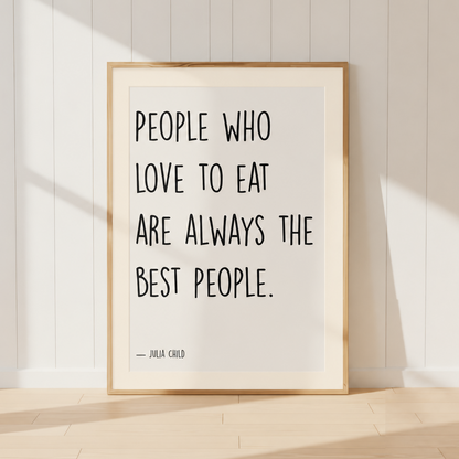 Julia Child quote print featuring "People Who Love To Eat Are Always The Best People" in a light oak frame with a warm ivory mount, styled in a cosy French country kitchen.