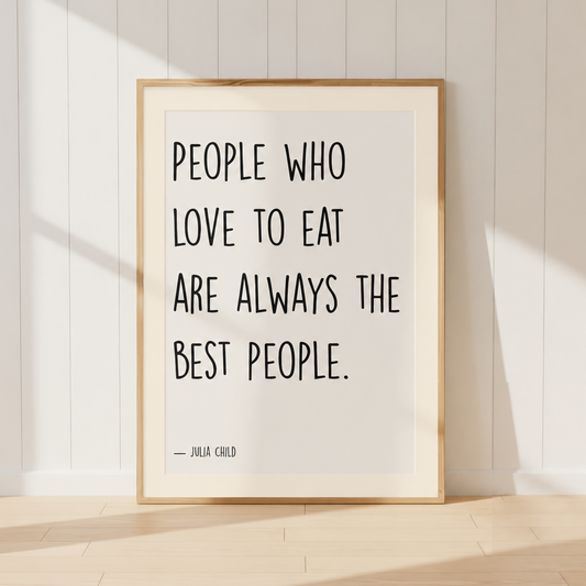 Julia Child quote print featuring "People Who Love To Eat Are Always The Best People" in a light oak frame with a warm ivory mount, styled in a cosy French country kitchen.