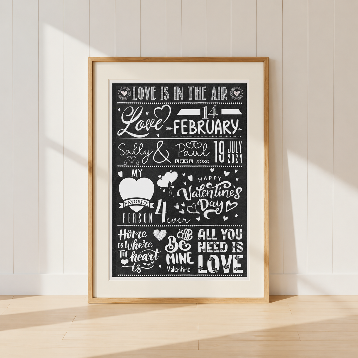 Personalised Valentine's Day typography print featuring names and dates in a black and white chalkboard style with a warm ivory mount and natural oak frame.