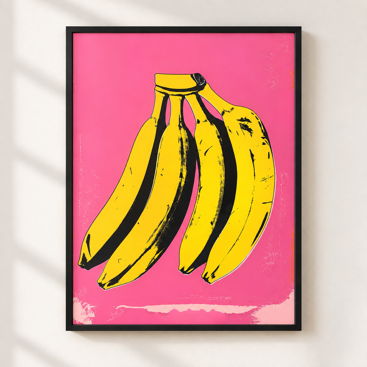 A framed pop-art style print featuring a bunch of yellow bananas on a bright pink background, hung on a light wall with soft shadow overlays.