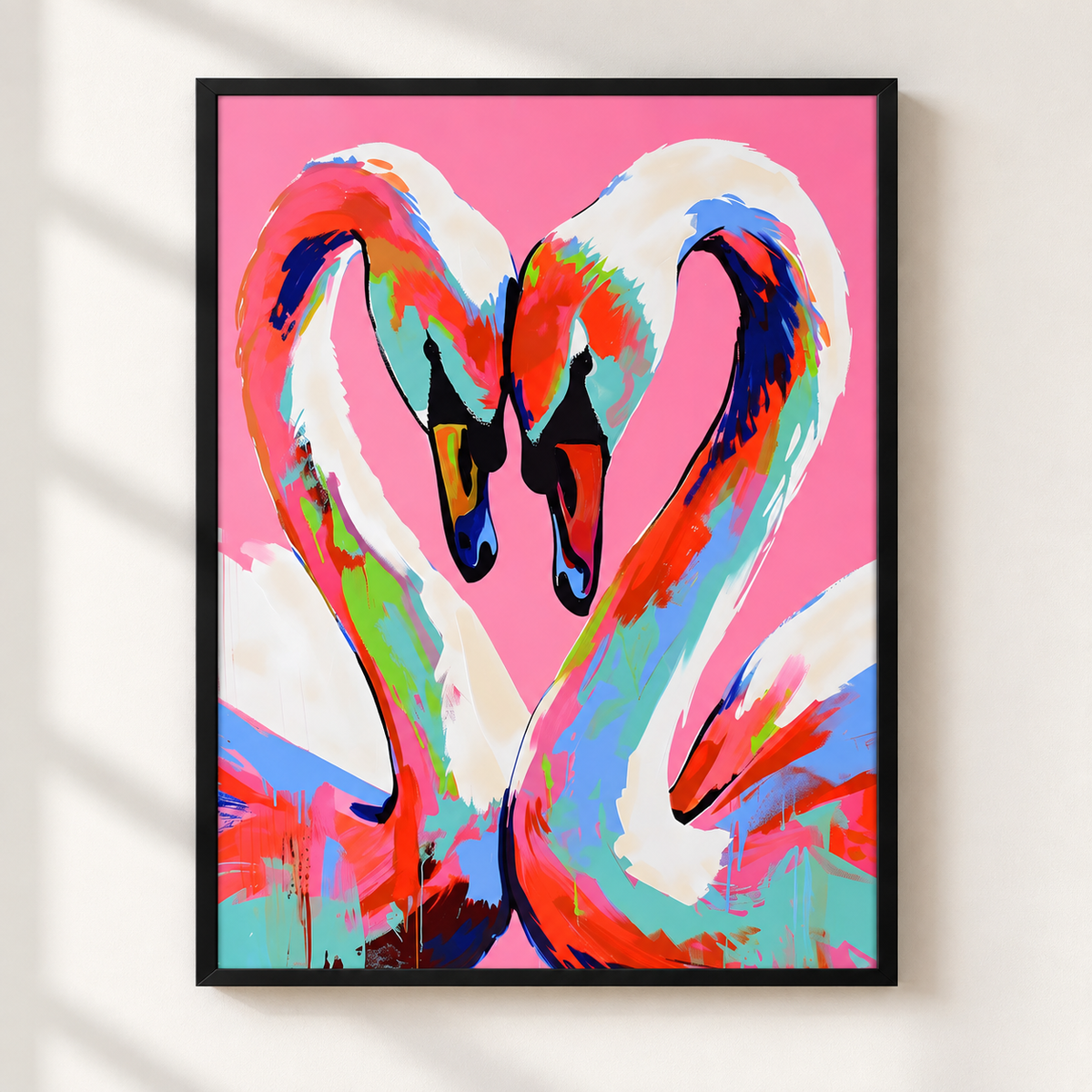 A framed pop-art style print of two swans forming a heart shape with their necks, featuring bold pink, white, red, blue, and green brushstrokes, displayed on a light wall.