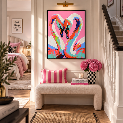 A colorful framed wall art print of two swans forming a heart shape, displayed in a bright, modern hallway above a white boucle bench with pink pillows and books.