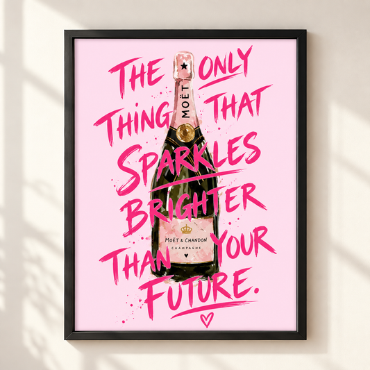 A framed art print featuring a pink background with a watercolor-style Moët & Chandon champagne bottle and bold pink handwritten text that reads, 'THE ONLY THING THAT SPARKLES BRIGHTER THAN YOUR FUTURE.' The print is shown hanging on a light beige wall with soft shadow patterns.