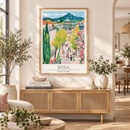 A framed travel art print of Seoul, South Korea, hanging on a beige wall in a modern, sunlit living room with a wooden console table and plants.