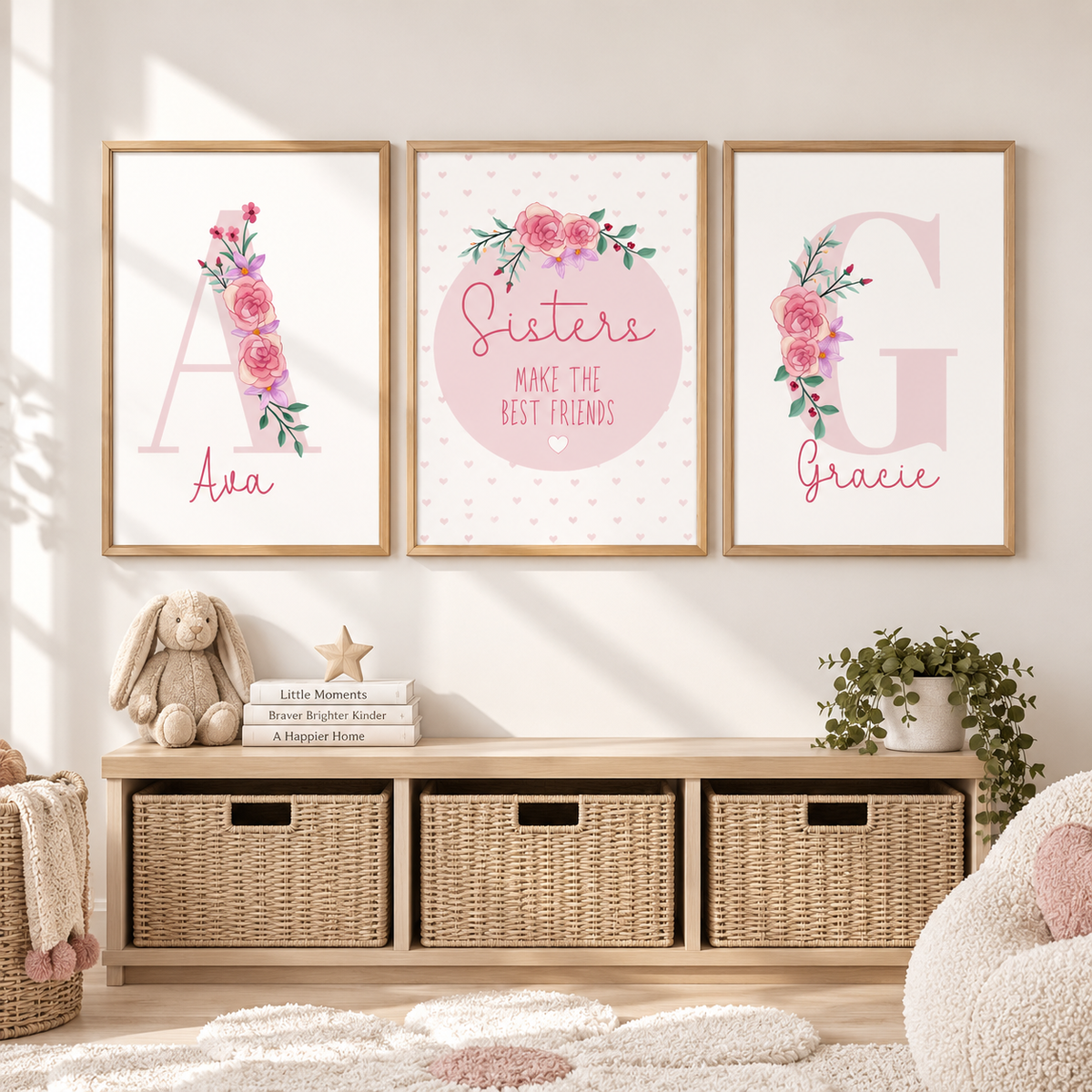 Three framed personalized nursery art prints hang on a white wall above a wooden storage bench with wicker baskets. The prints feature floral letter designs: 'A Ava' on the left, 'Sisters MAKE THE BEST FRIENDS' in the center, and 'G Gracie' on the right.