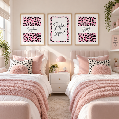 A styled bedroom with two twin beds, pink bedding, and three framed wall prints above the beds. The prints feature pink leopard print sections with the names Sophie, Sister Squad, and Natalie in black script.