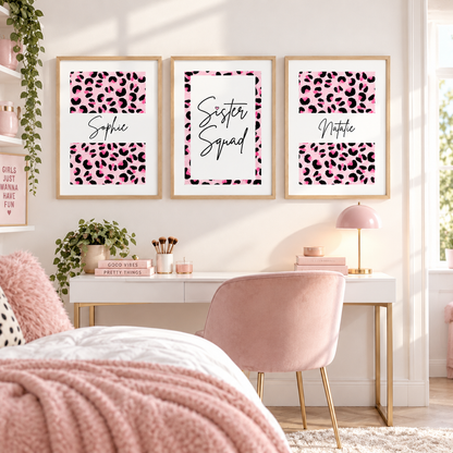 Three framed personalized leopard print wall art prints hang above a white desk in a styled bedroom. The prints feature pink and black leopard patterns with the names Sophie, Sister Squad, and Natalie.