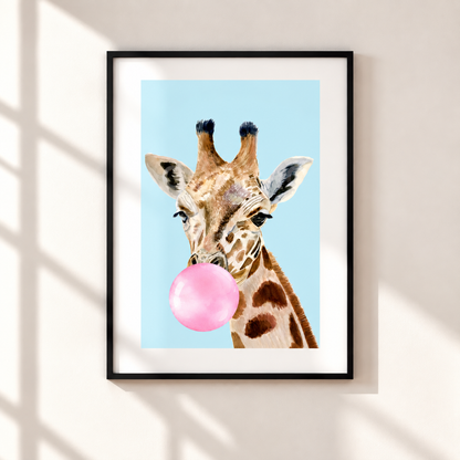 A framed art print featuring a watercolor-style giraffe blowing a pink bubblegum bubble against a light blue background, mounted on a beige wall with soft window shadow patterns.