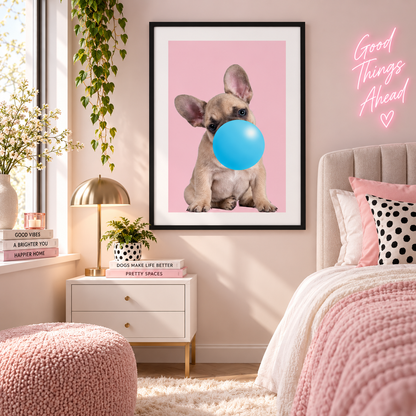 A framed wall art print featuring a light brown French Bulldog sitting against a pink background and blowing a bright blue bubblegum bubble, displayed in a styled bedroom setting.