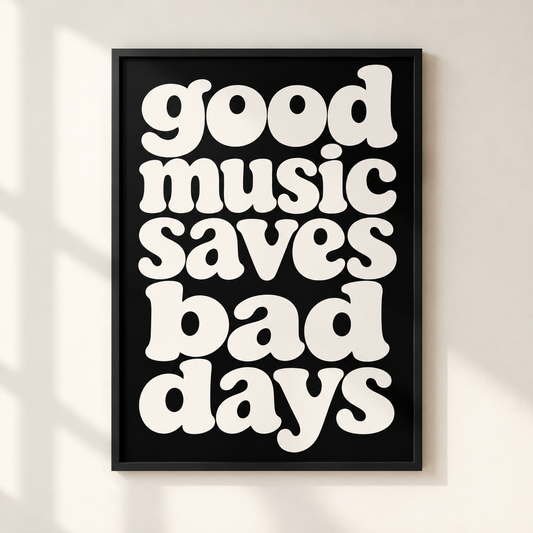 A framed typographic wall art print with the phrase “good music saves bad days” in large white retro letters on a black background, hanging on a light wall with soft shadow overlays.