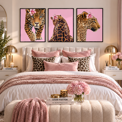A styled bedroom featuring a three-panel framed wall art set of leopards on a pink background, hung above a bed with pink and leopard-print pillows, blush bedding, and matching decor.