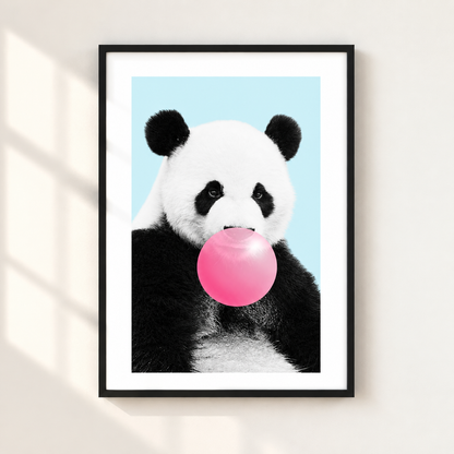 A framed art print featuring a panda with black and white fur blowing a bright pink bubblegum bubble against a light blue background, displayed on a beige wall with soft window shadow overlays.