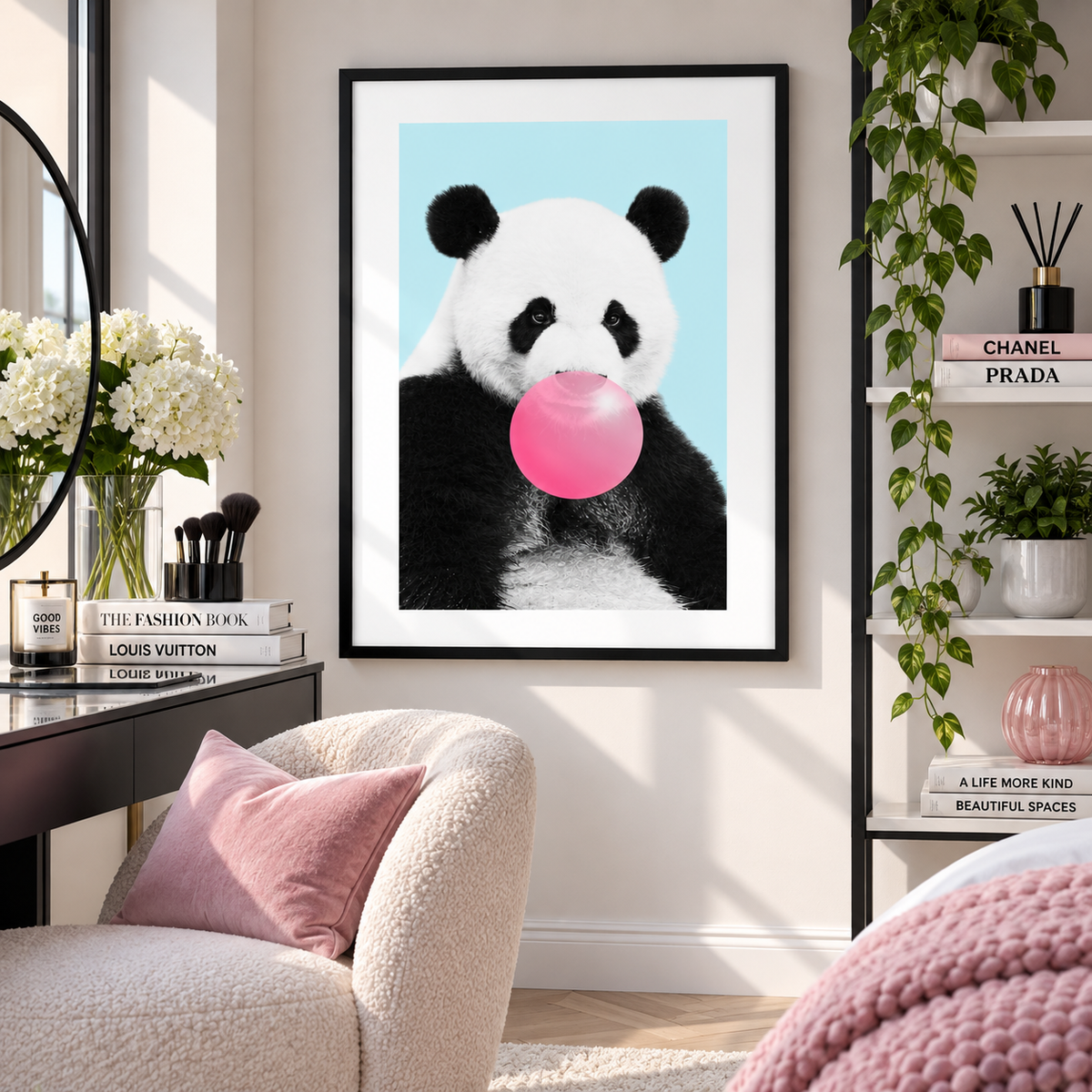 A framed wall art print featuring a panda holding a pink bubblegum bubble, displayed in a styled room setting above a beige armchair with a pink pillow.