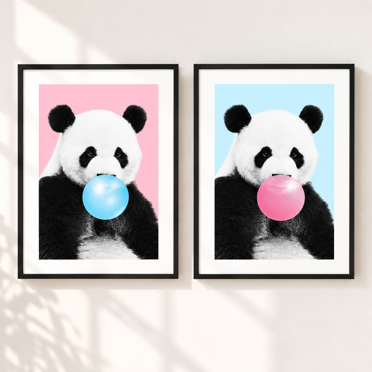 Two framed panda wall art prints hang side by side on a light wall. Each print shows a black-and-white panda holding a bubblegum bubble: one blue and one pink, against pink and light blue backgrounds respectively.