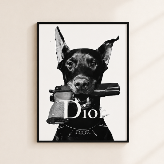 A framed black and white art print of a Doberman dog holding a gun with the word 'Dior' across the center, hanging on a beige wall with soft diagonal shadows.
